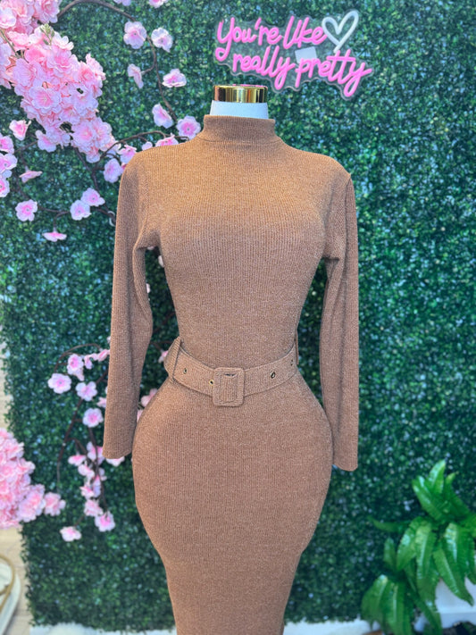 Mannequin wearing a brown ribbed dress with a belt against a decorative background with pink flowers and greenery.